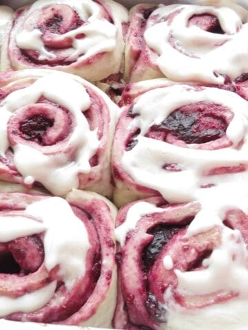 Mixed berry sweet rolls finished in pan with cream cheese frosting on top.