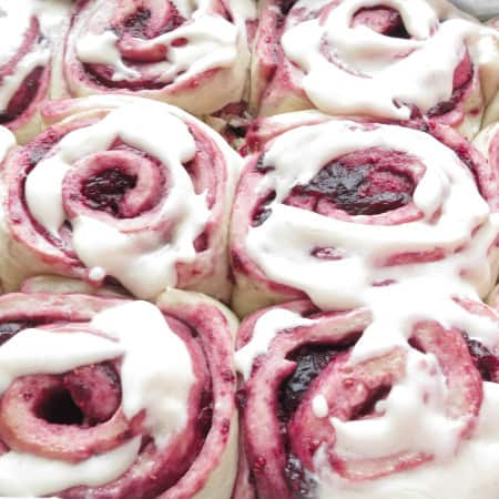 Mixed berry sweet rolls finished in pan with cream cheese frosting on top.