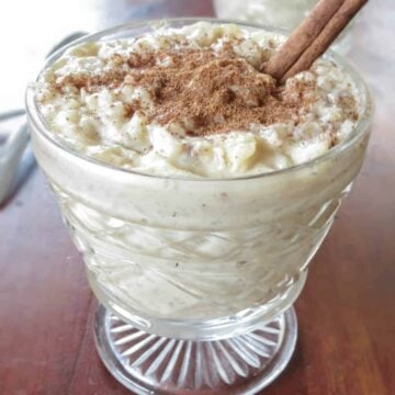 Homemade creamy rice pudding in a clear glass cup with cinnamon sprinkled on top and a cinnamon stick stuck in.