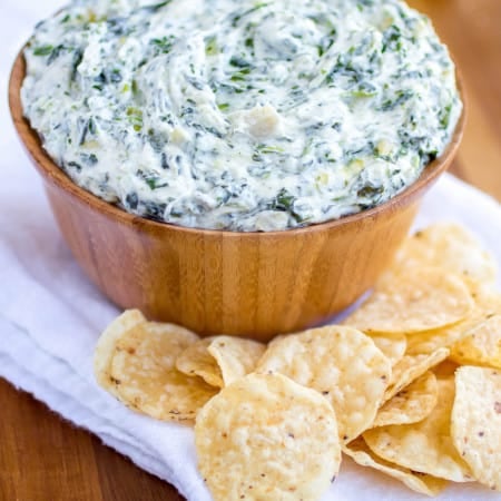 Spinach and artichoke dip in a wood bowl with chips surrounding it.