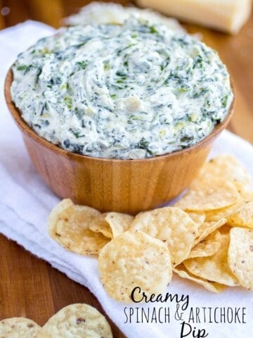 Spinach and artichoke dip in a wood bowl with chips surrounding it.