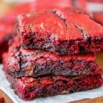 Red velvet brownies stacked on top of one another with a bite taken out of the top one.