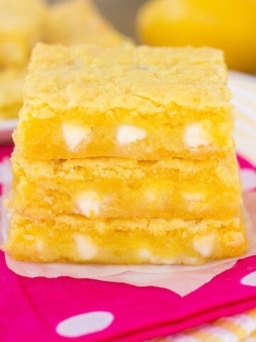 Lemon Gooey bars stacked on a pink napkin.