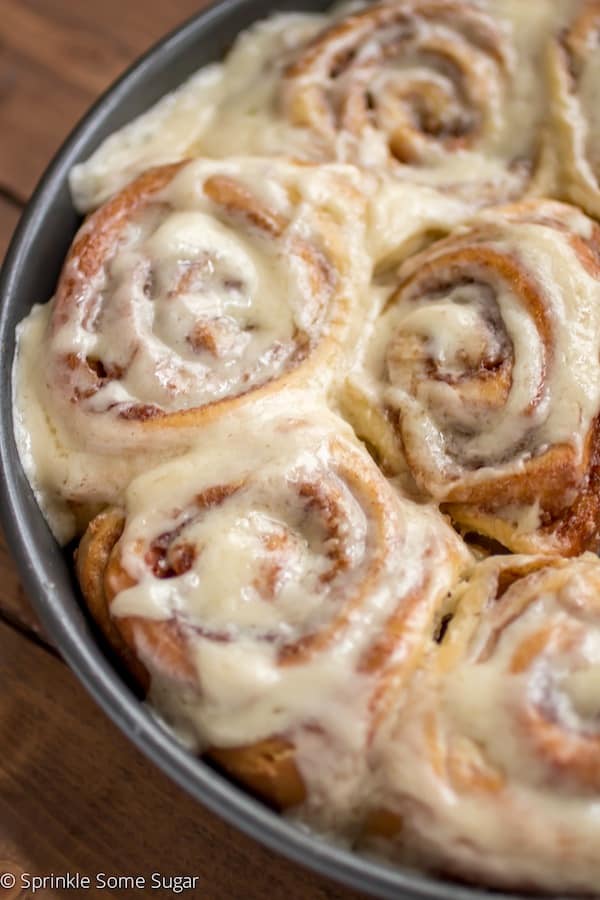 Soft and fluffy cinnamon rolls in pan after baking with cream cheese frosting.