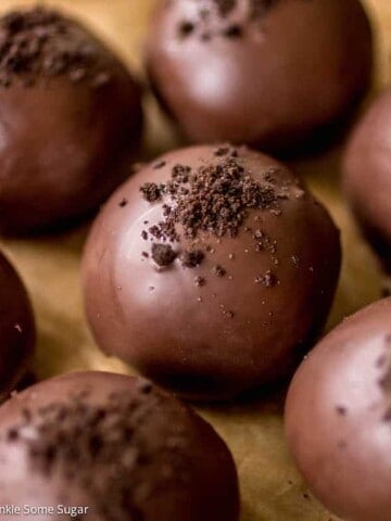 Oreo truffles on brown parchment paper covered in chocolate and Oreo crumbs sprinkled on top.