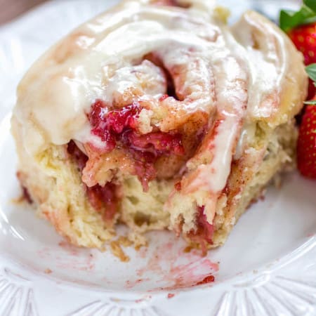 Strawberry cinnamon rolls on a plate with a bite taken out.
