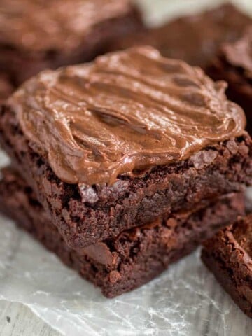 Chewy Frosted Brownies stacked on parchment paper.