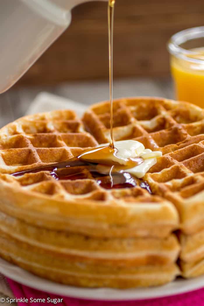 Stack of buttermilk waffles with syrup pouring on top.