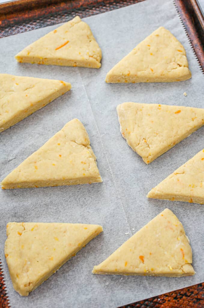Orange scone dough triangles on a baking sheet before baking.