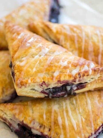 Stack of gooey blueberry turnovers with glaze on top.