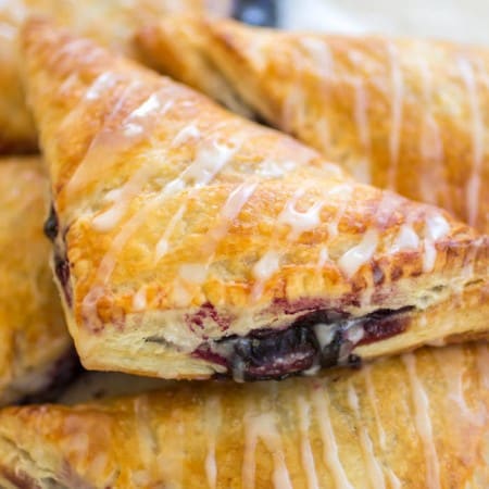 Stack of gooey blueberry turnovers with glaze on top.