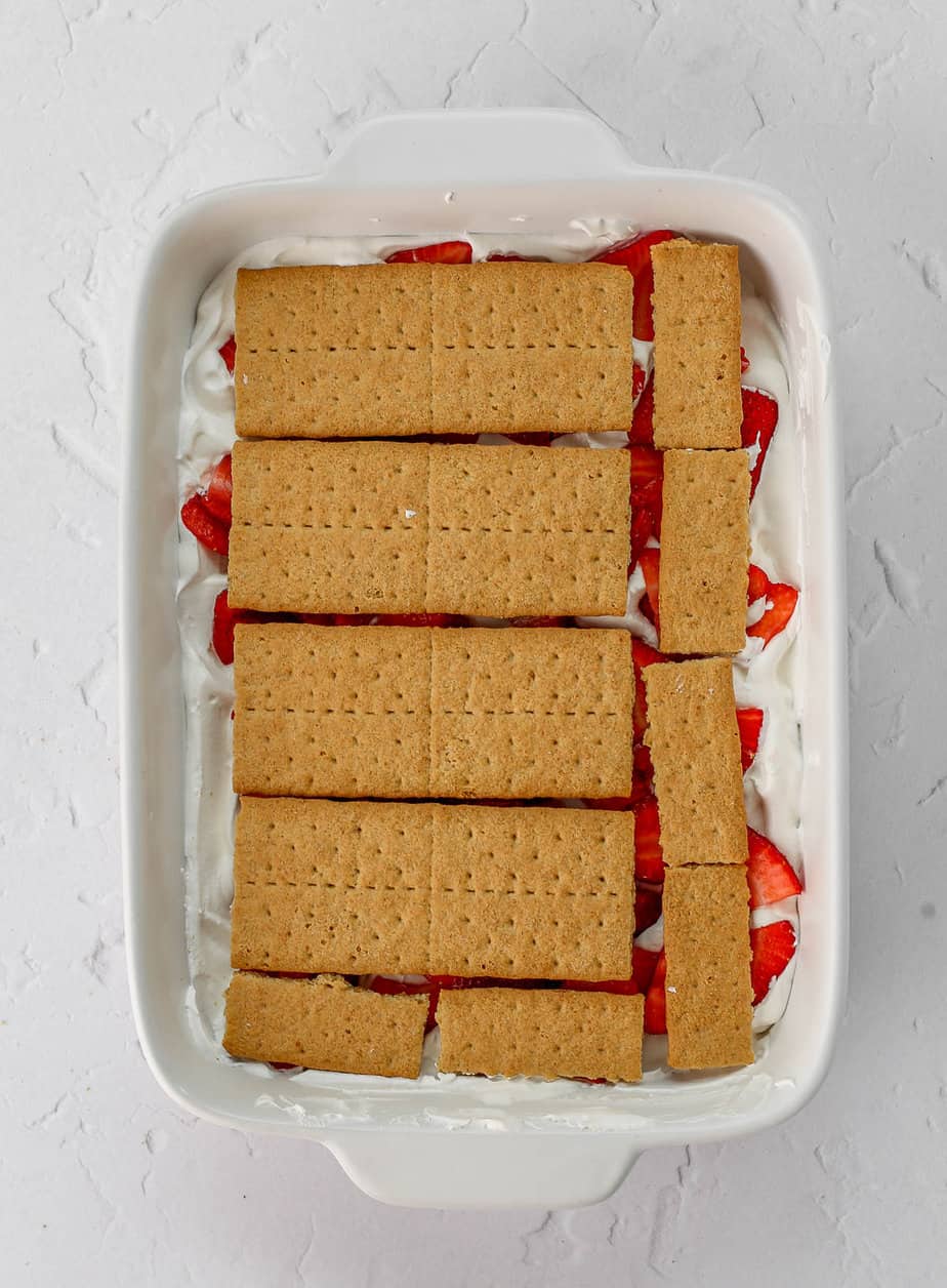 Layers of strawberries, whipped cream and graham crackers in a baking dish.