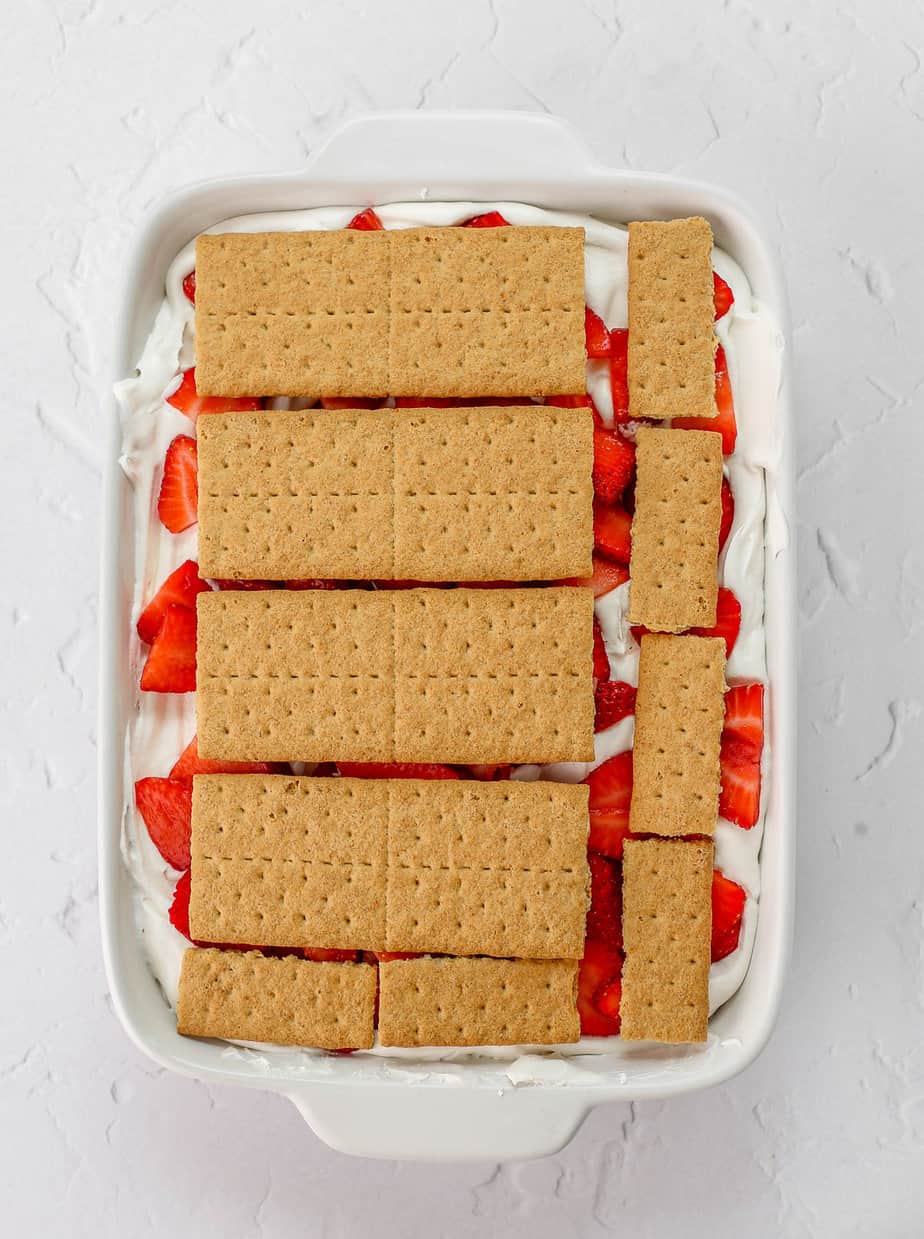 Layers of strawberries, whipped cream and graham crackers in a baking dish.