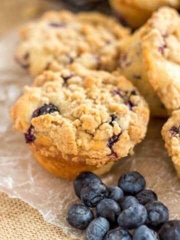 Blueberry muffin with crumb topping on a piece of parchment paper.