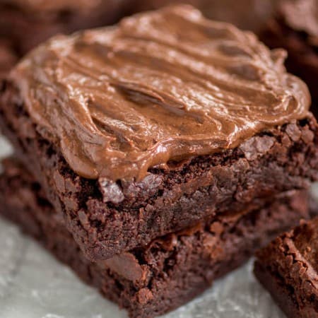 Chewy Frosted Brownies stacked on parchment paper.