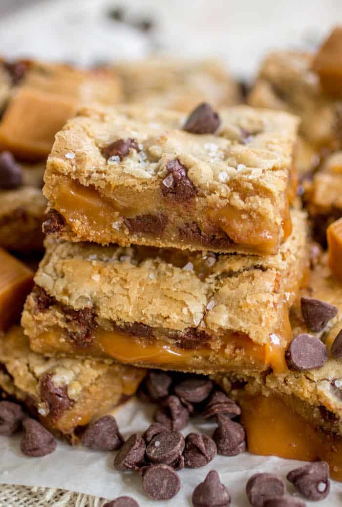 Salted caramel chocolate chip cookie bars stacked on top of one another on white parchment paper.