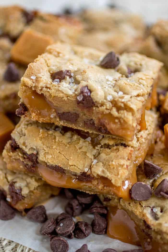 Salted caramel chocolate chip cookie bars stacked on top of one another on white parchment paper.