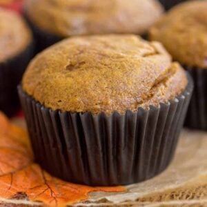 Pumpkin cheesecake swirl muffin with a dark brown wrapping sitting atop of an orange leaf.