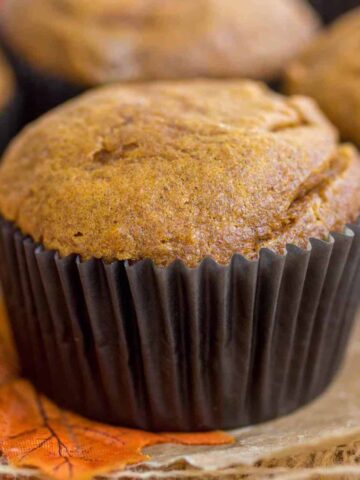 Pumpkin cheesecake swirl muffin with a dark brown wrapping sitting atop of an orange leaf.