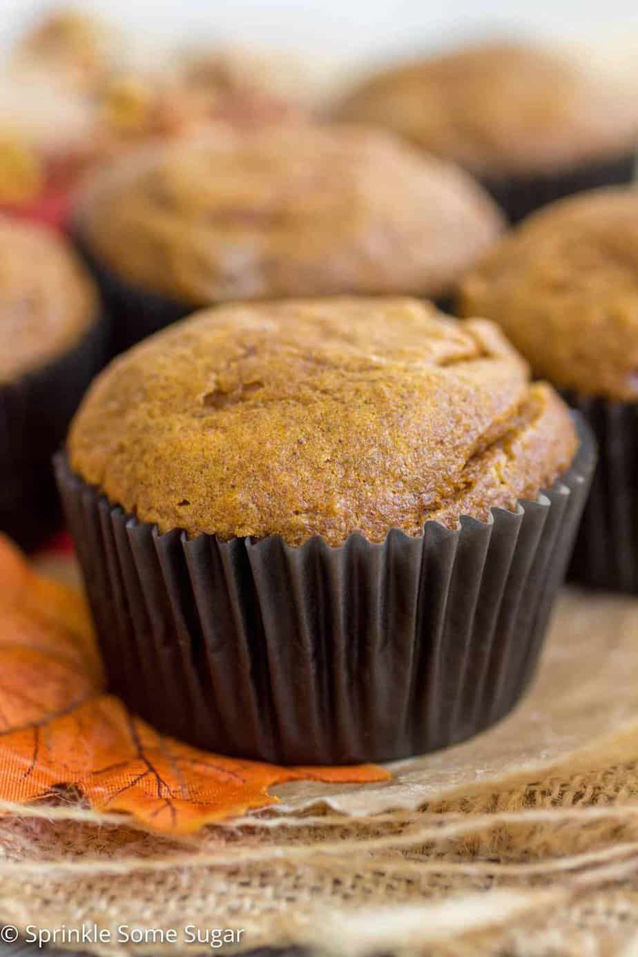 Pumpkin cheesecake swirl muffin with a dark brown wrapping sitting atop of an orange leaf.