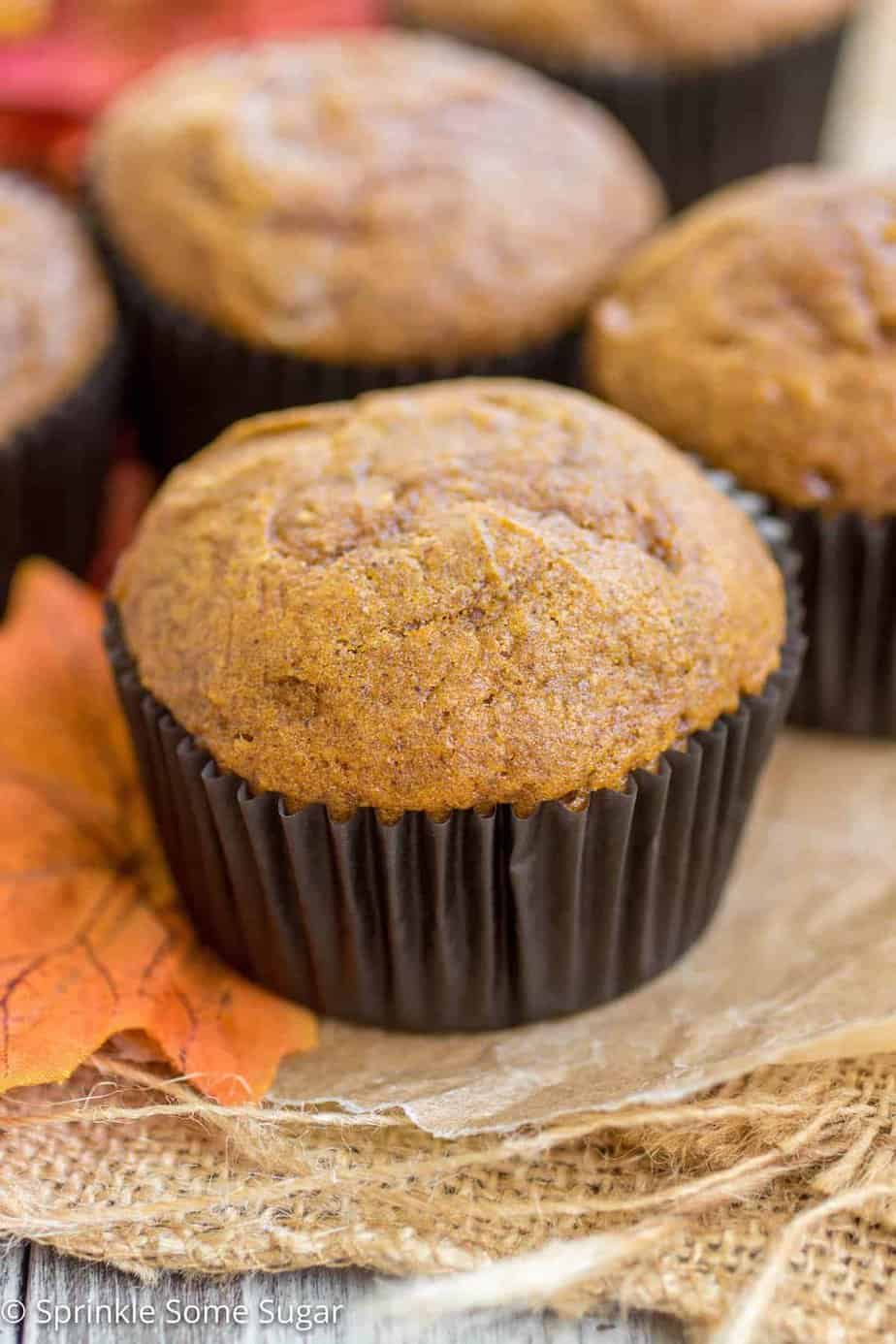 Pumpkin cheesecake swirl muffin with a dark brown wrapping sitting atop of an orange leaf.