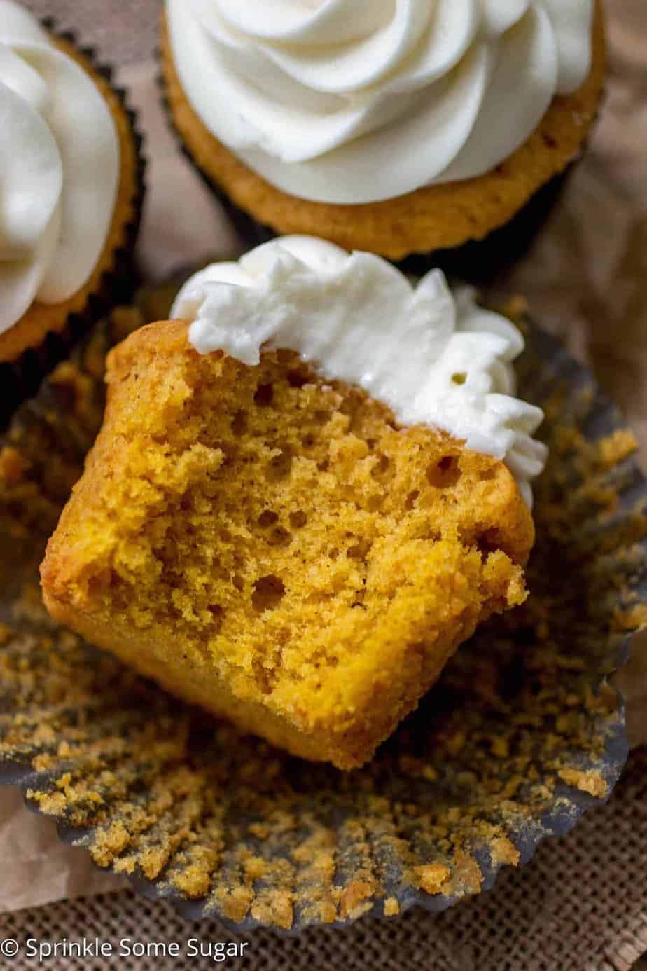 Pumpkin spice cupcakes on a piece or brown parchment paper lying down with a bite taken out.