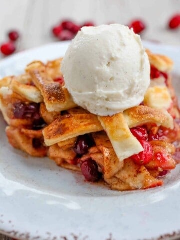 Cranberry Apple Pie with a scoop of vanilla ice cream on top on a plate.