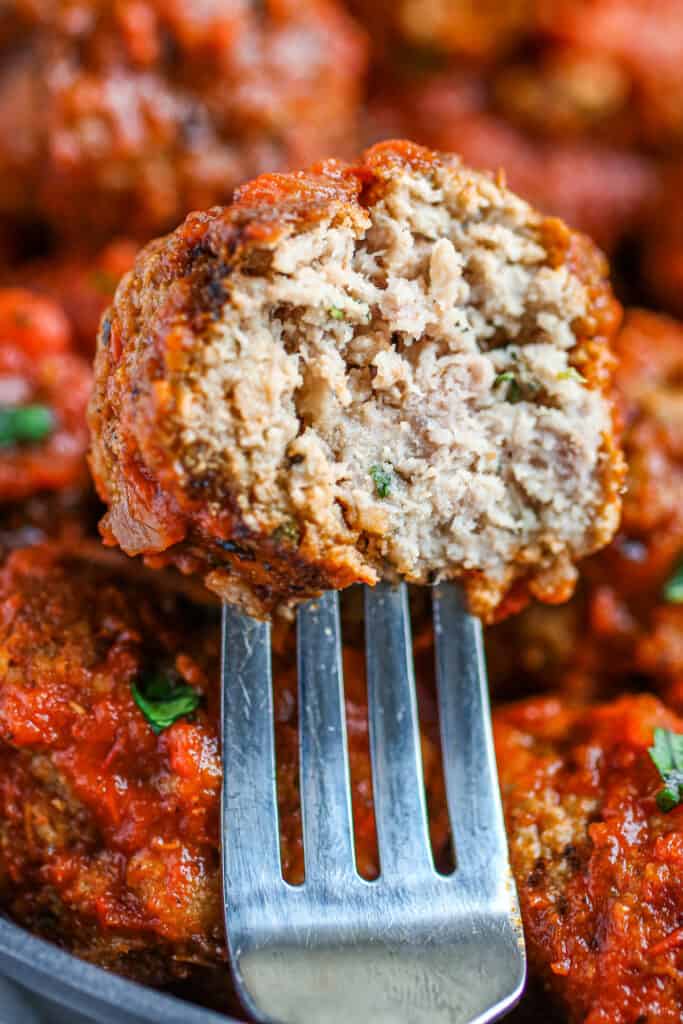 Meatball half bitten to reveal tender inside on a fork.