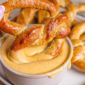 Baked soft pretzel being dipped into beer cheese dip.