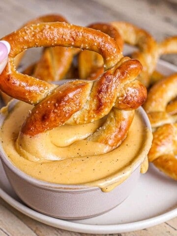 Baked soft pretzel being dipped into beer cheese dip.
