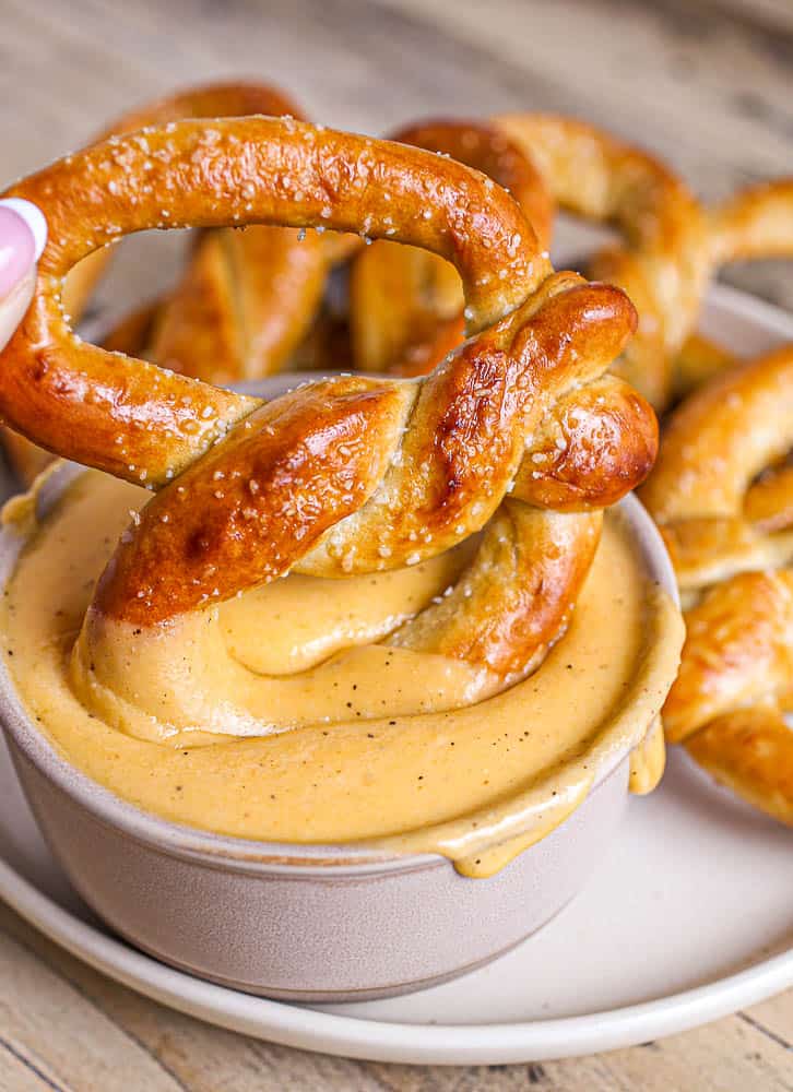 Baked soft pretzel being dipped into beer cheese dip.