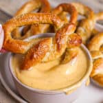 Soft pretzel being dipped into beer cheese dip for pretzels.