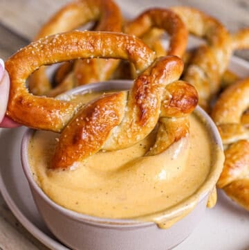 Soft pretzel being dipped into beer cheese dip for pretzels.