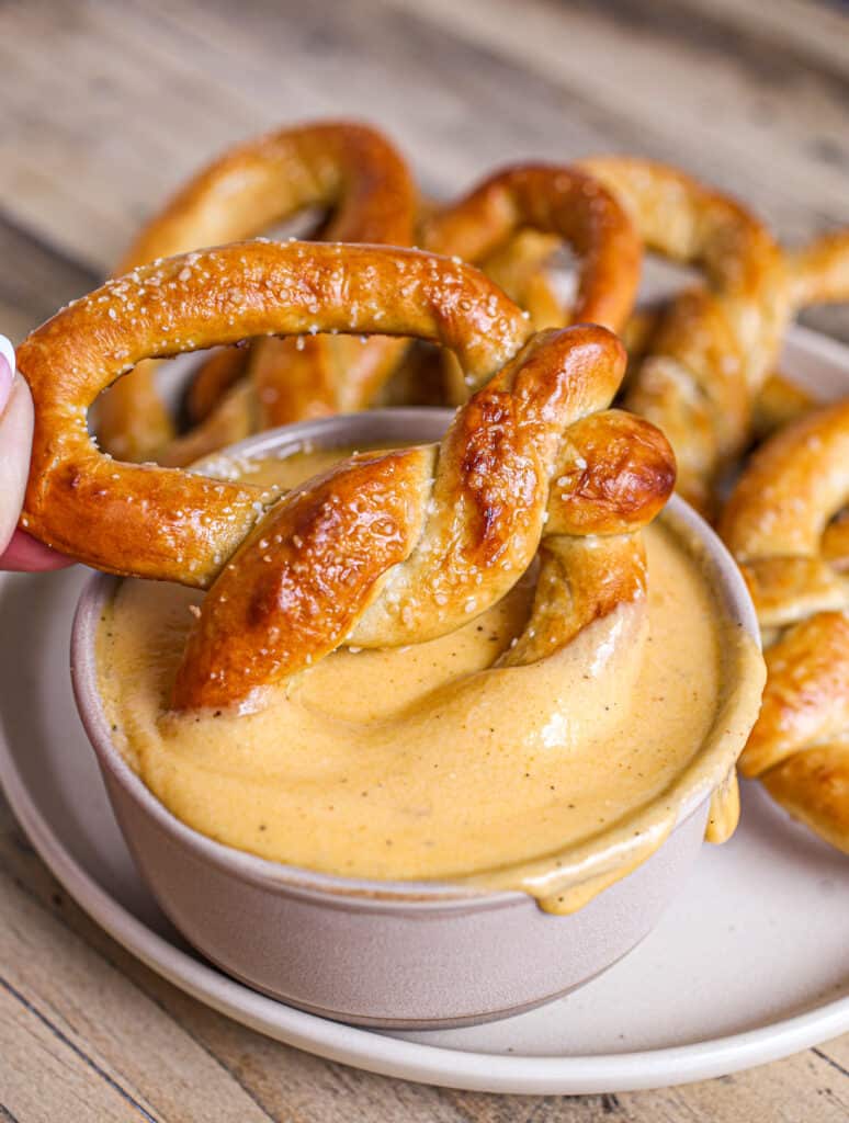 Soft pretzel being dipped into beer cheese dip for pretzels.