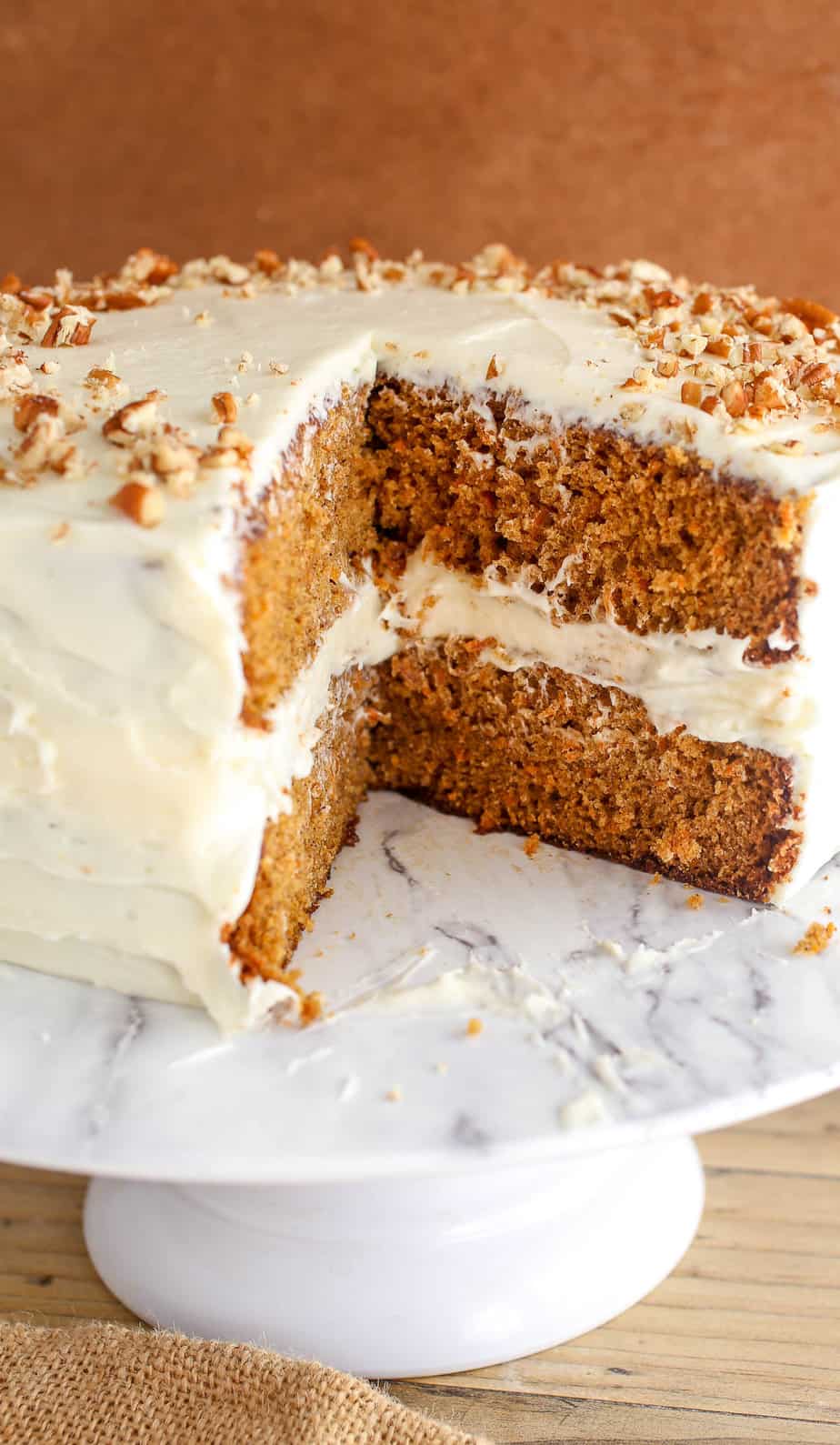 Carrot cake on a cake stand with a slice missing.