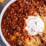 Classic bowl of chili recipe with a dollop of sour cream and melted cheese on top.