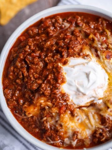 Classic bowl of chili recipe with a dollop of sour cream and melted cheese on top.