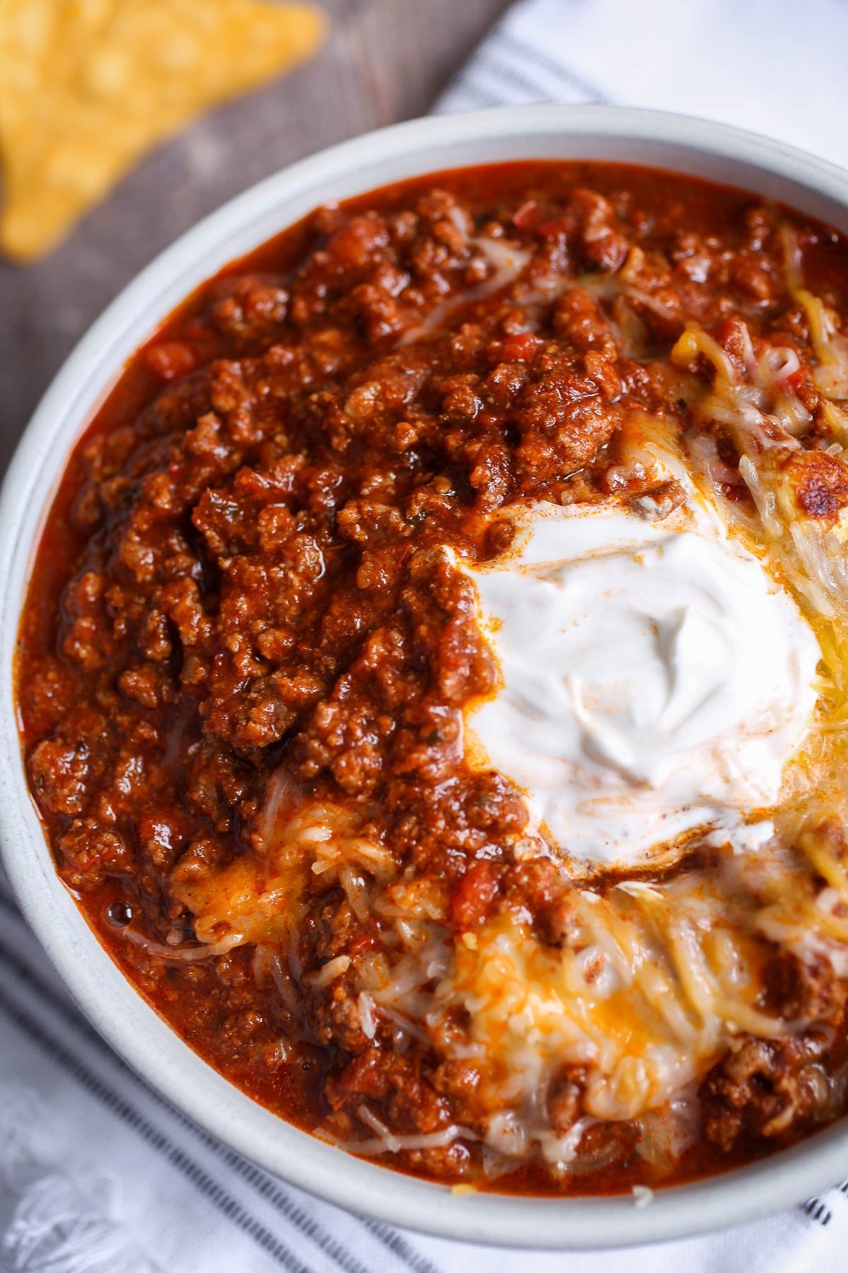 Classic bowl of chili recipe with a dollop of sour cream and melted cheese on top.